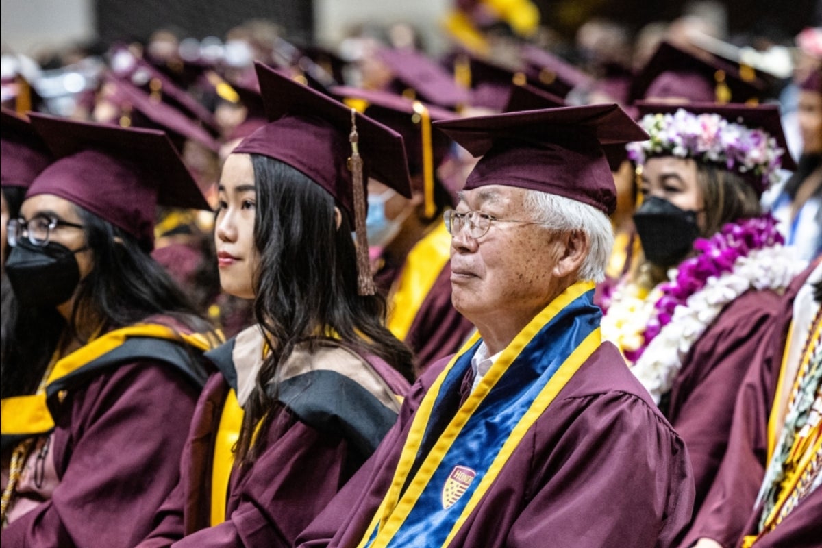 Graduates in caps and gowns sit in an audience.