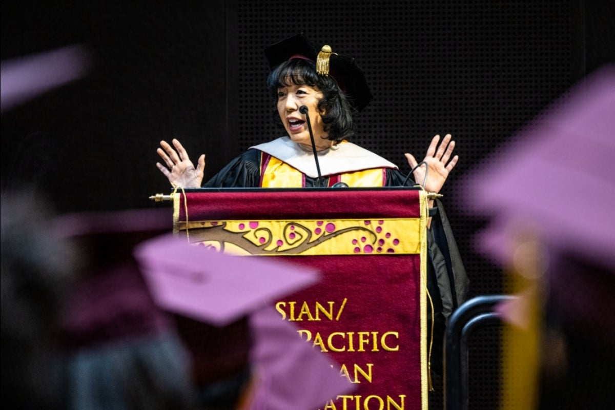 A woman raises her hands as she speaks behind a lectern