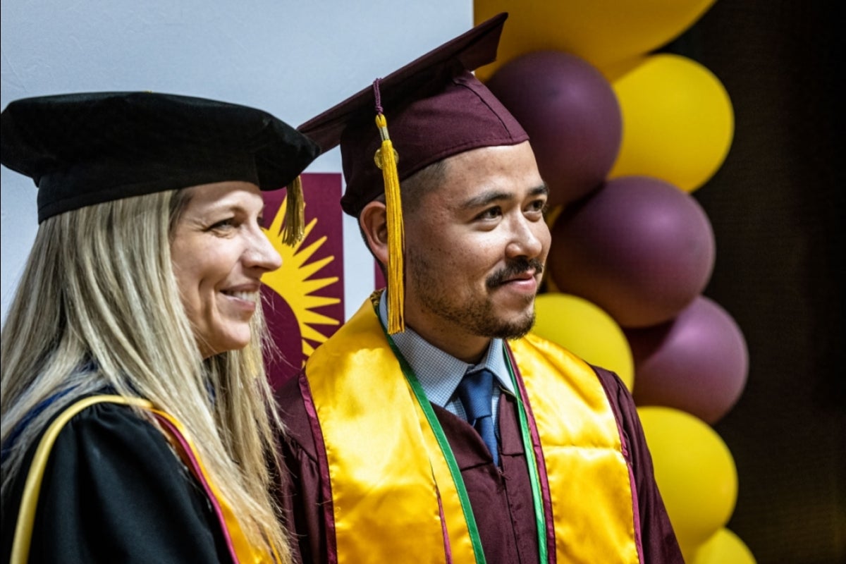 A man in graduation gown and cap poses for a photo next to a woman in academic regalia