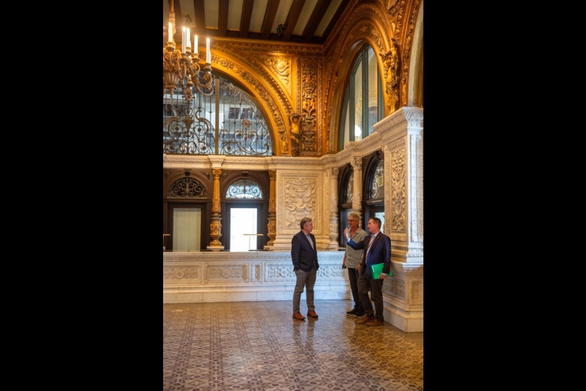 Three men stand in an ornate lobby talking.