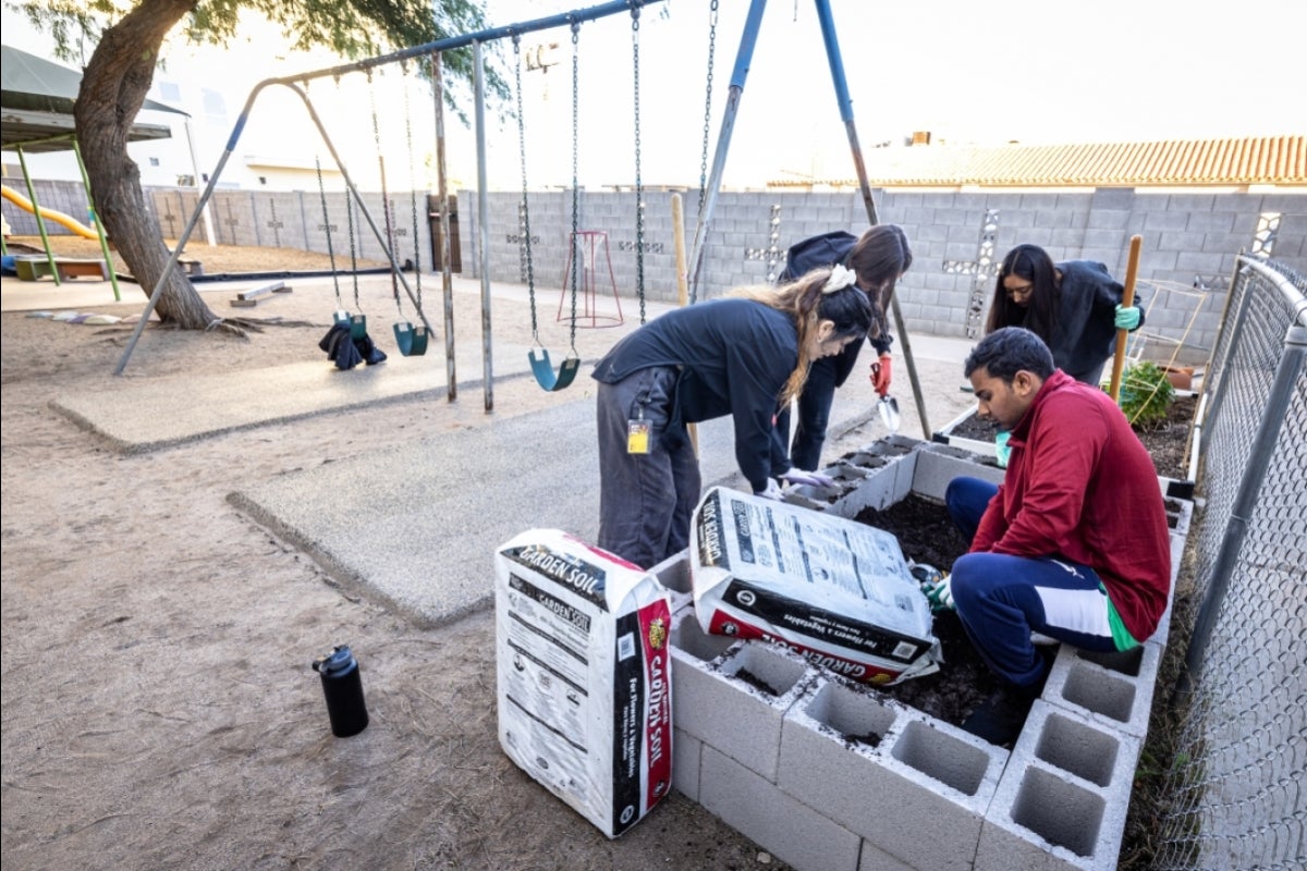 Students building a garden bed by a swingset