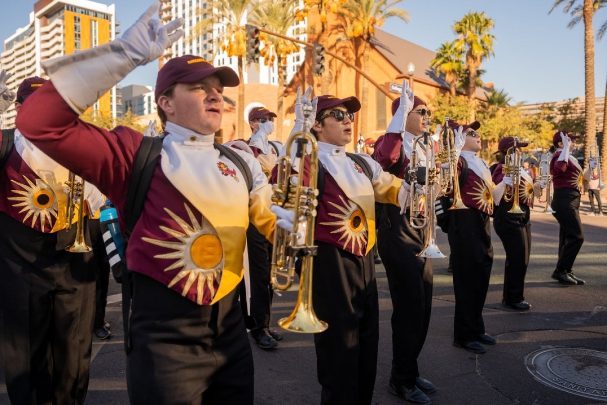 Marching band members gesture while holding trumpets during a parade