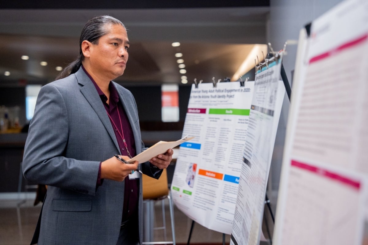 Man looking at posters while holding a stack of papers and a pen.