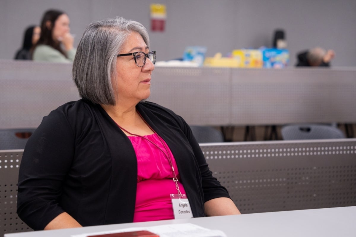 Woman seated at a desk, listening to a speaker.