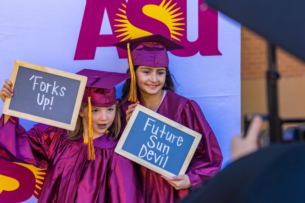 Two young girls have their pictures taken in maroon caps and gowns