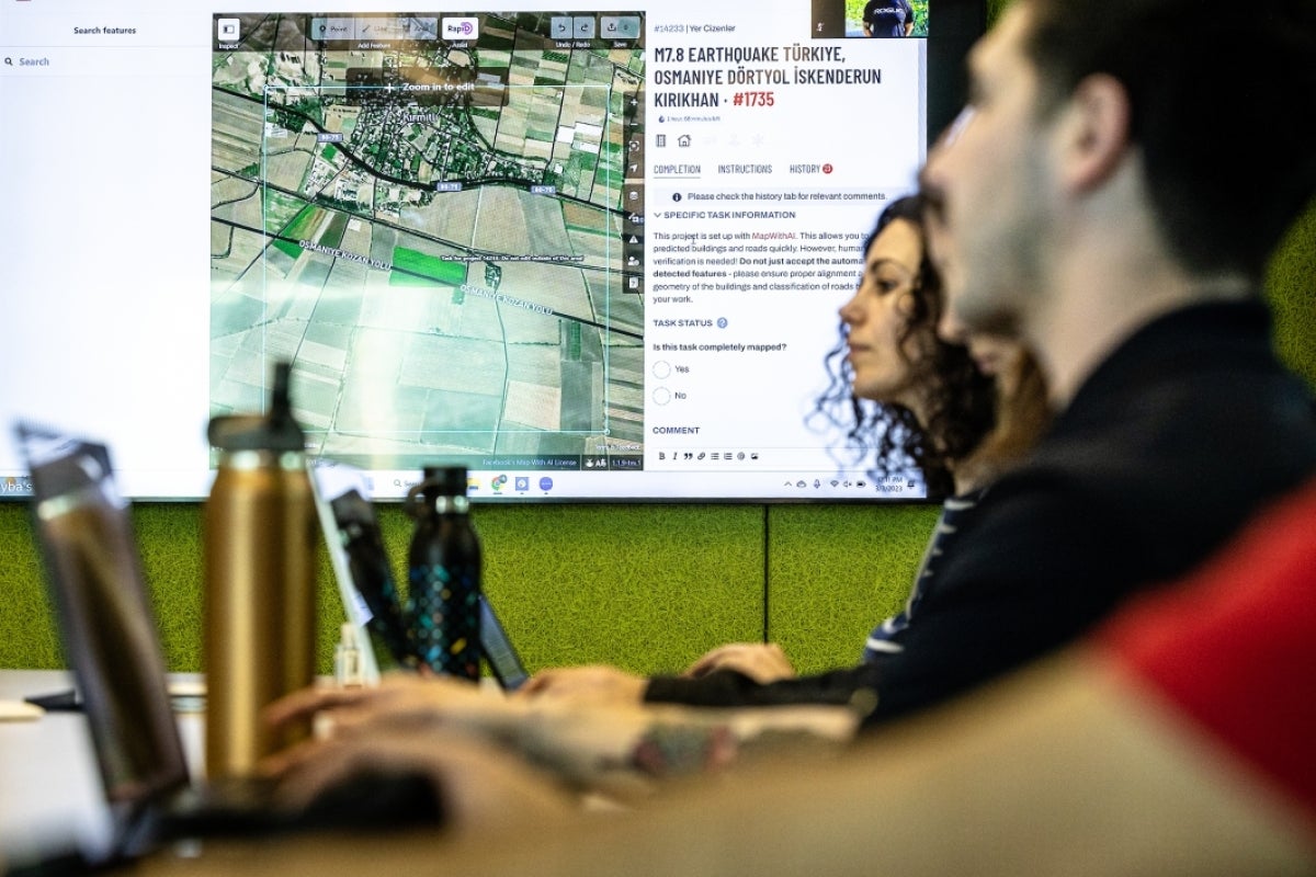 People working on laptops with map displayed on screen behind them