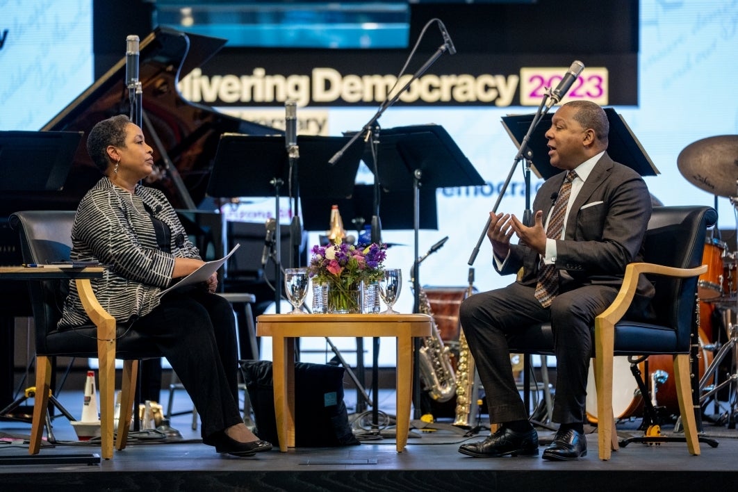 Two people sitting in chairs on stage talking during Delivering Democracy event