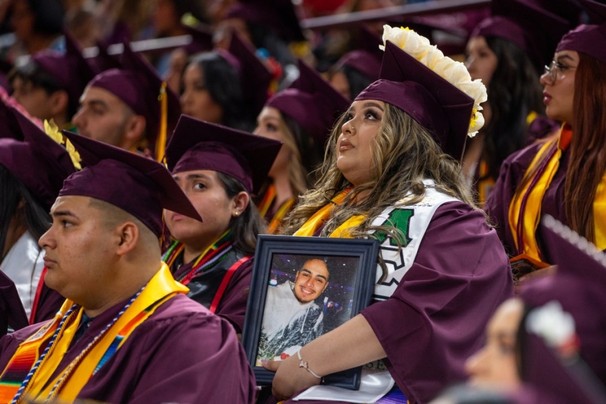 Graduate at convocation holding framed portrait of boyfriend