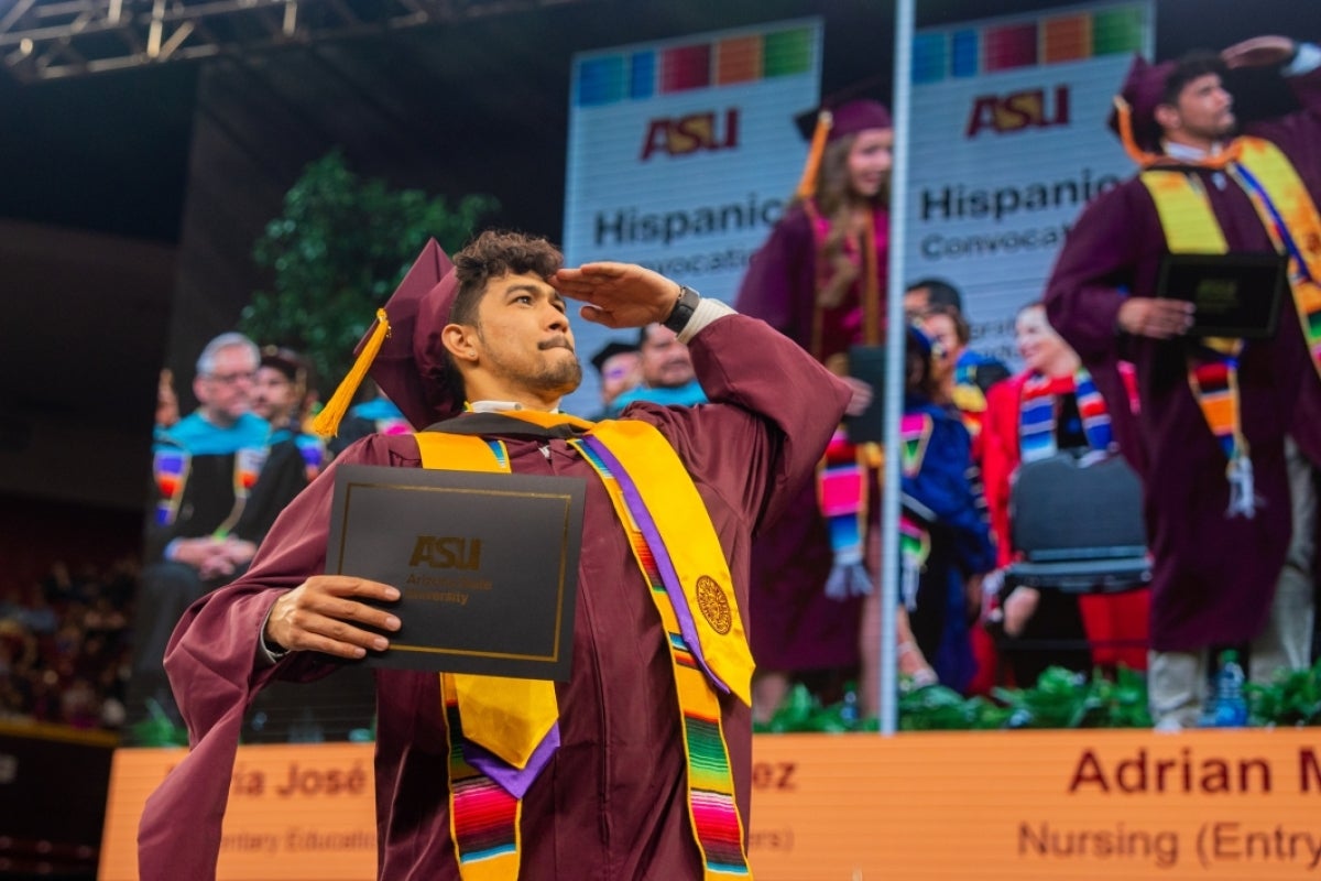 Graduate crossing stage holding diploma and saluting