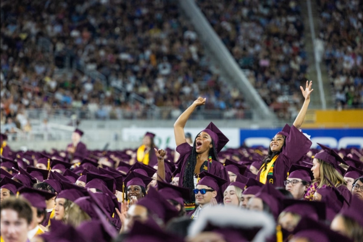 Two grads standing up from crowd and waving at commencement