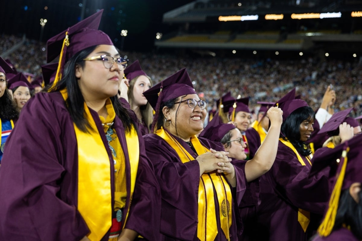 Two graduates standing with crowd and smiling at commencement