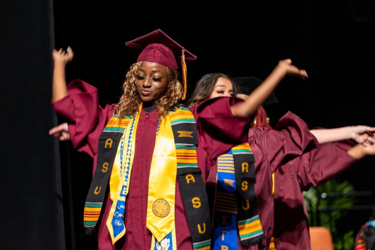 Three graduates dance as they cross the stage at convocation