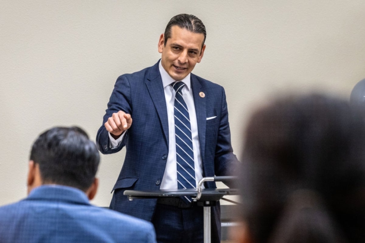 A man points at the audience as he speaks at a lectern