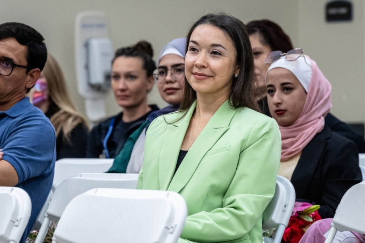 A woman sits in an audience smiling at the speaker off camera