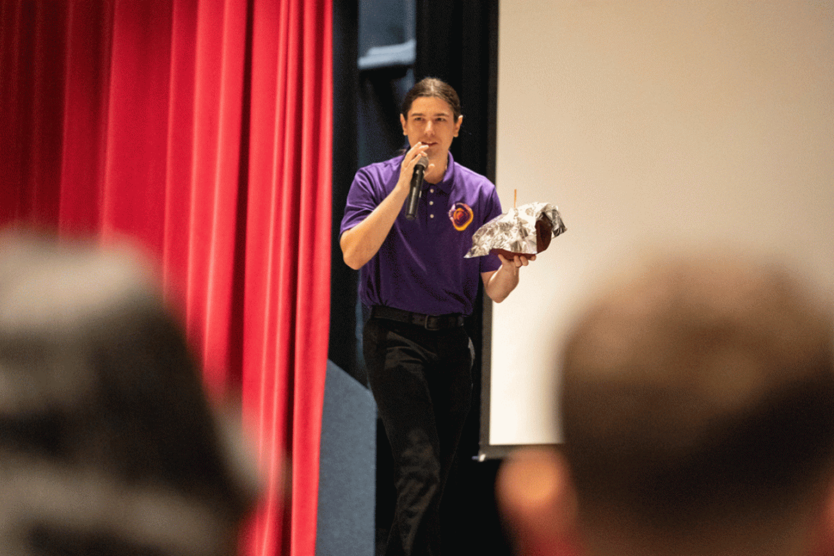 A man speaks onstage holding a football covered in aluminum foil