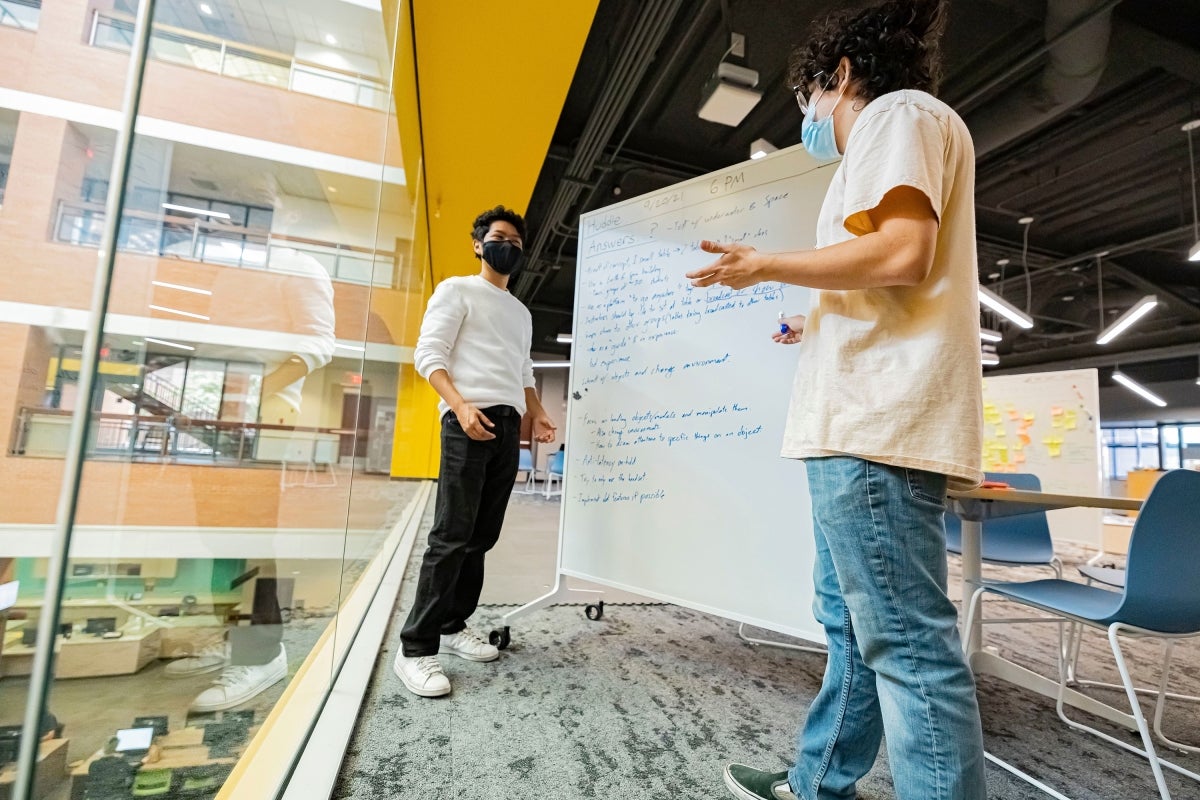 Two people storyboarding ideas on a whiteboard in a meeting room.