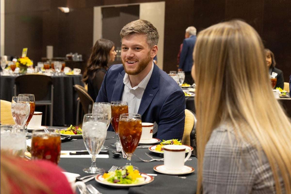 Man seated at a table smiling and talking to others around him.