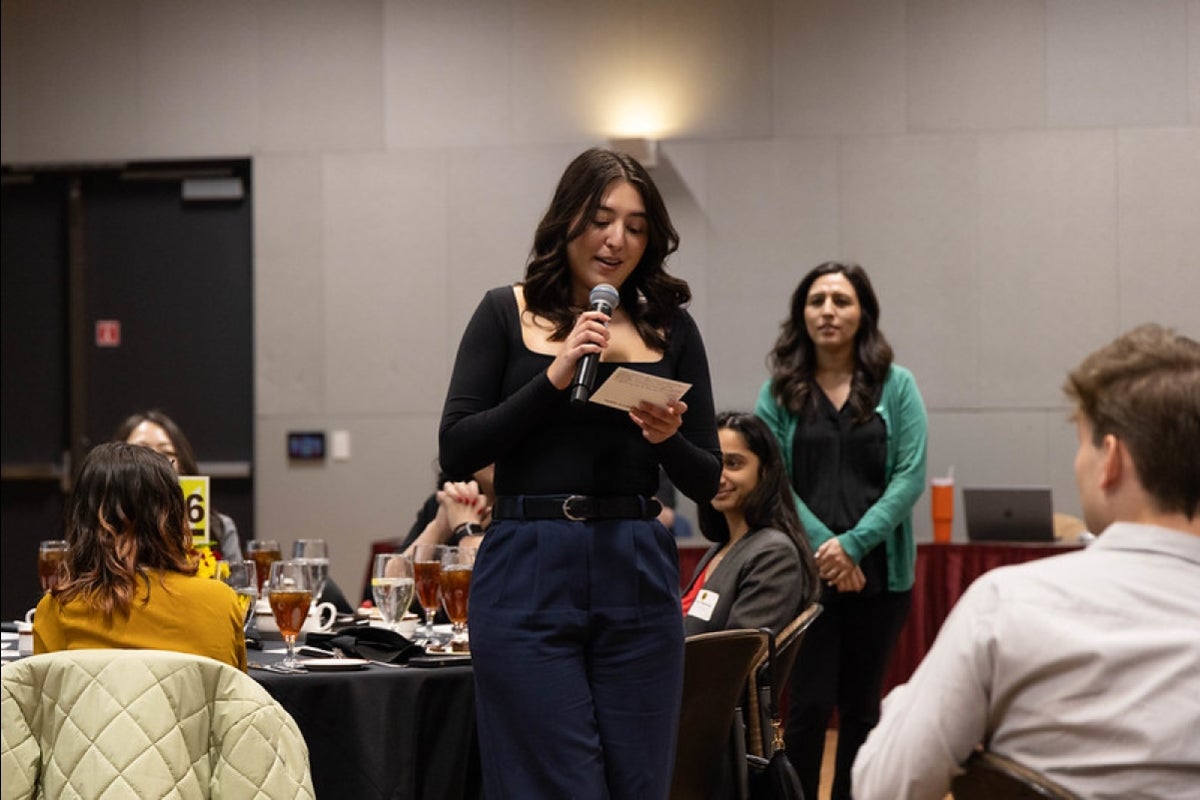 Woman holding a microphone speaking to an audience.