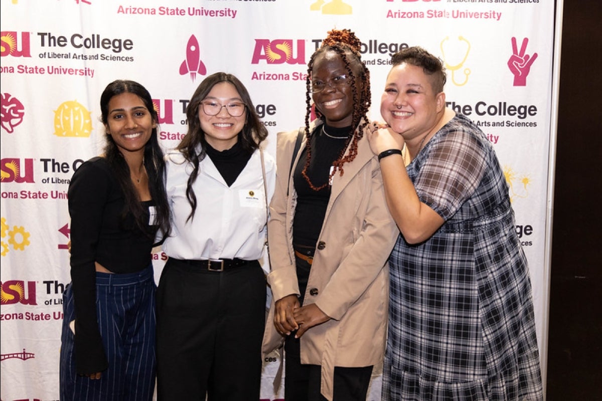 ASU students pose for a group photo in front of a backdrop with various ASU unit logos.