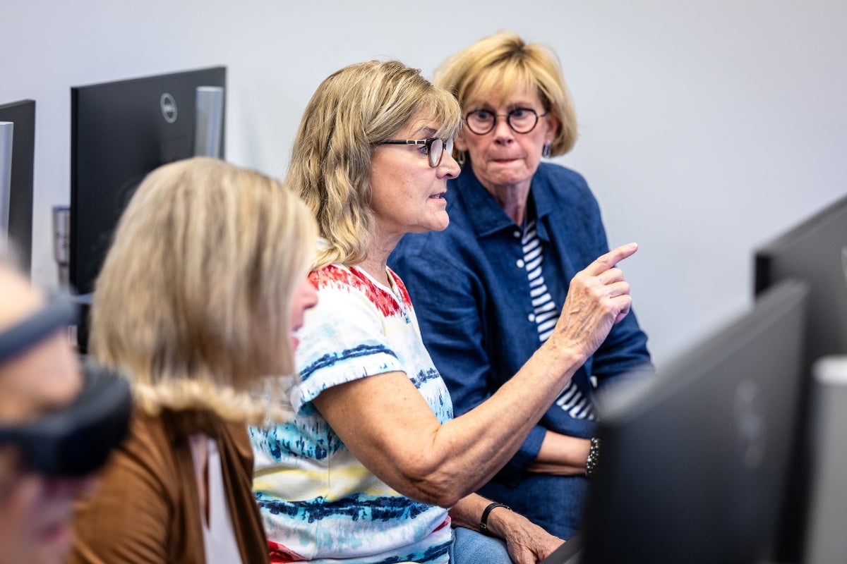 Three women work at computer screens in a classroom