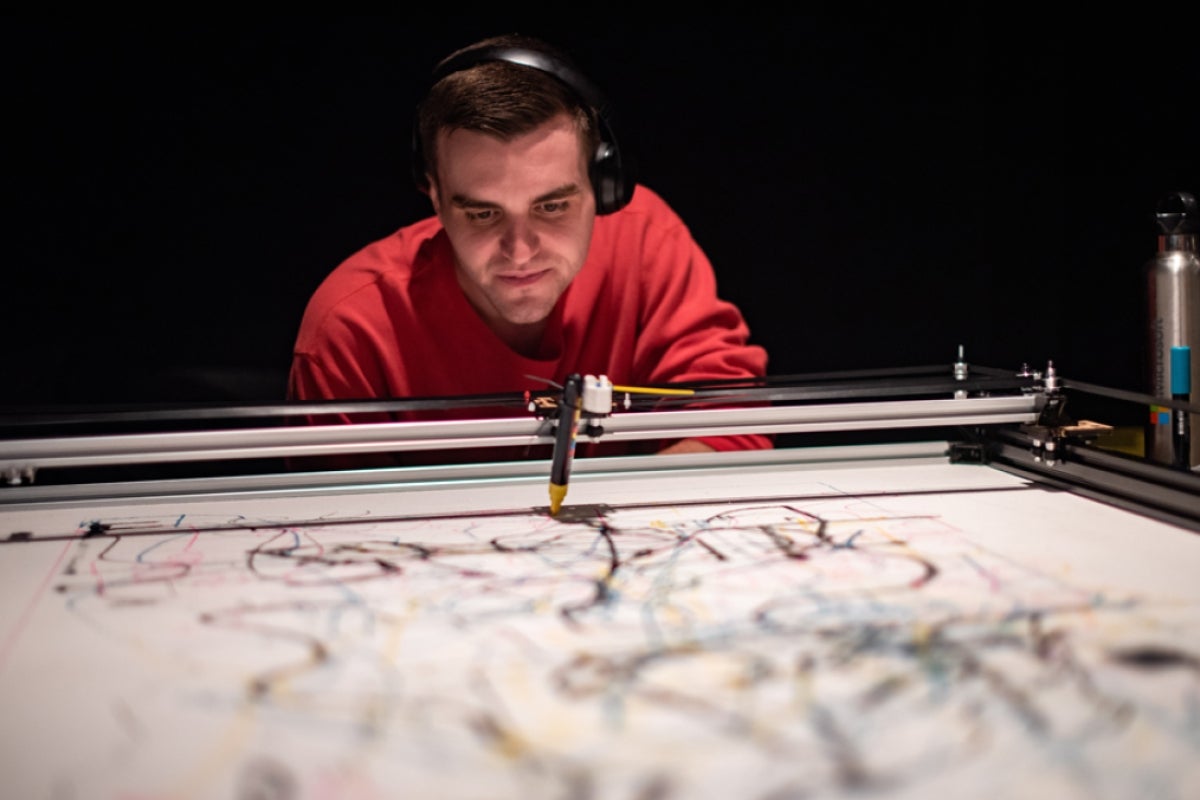 Man looking at a robotic arm creating art.