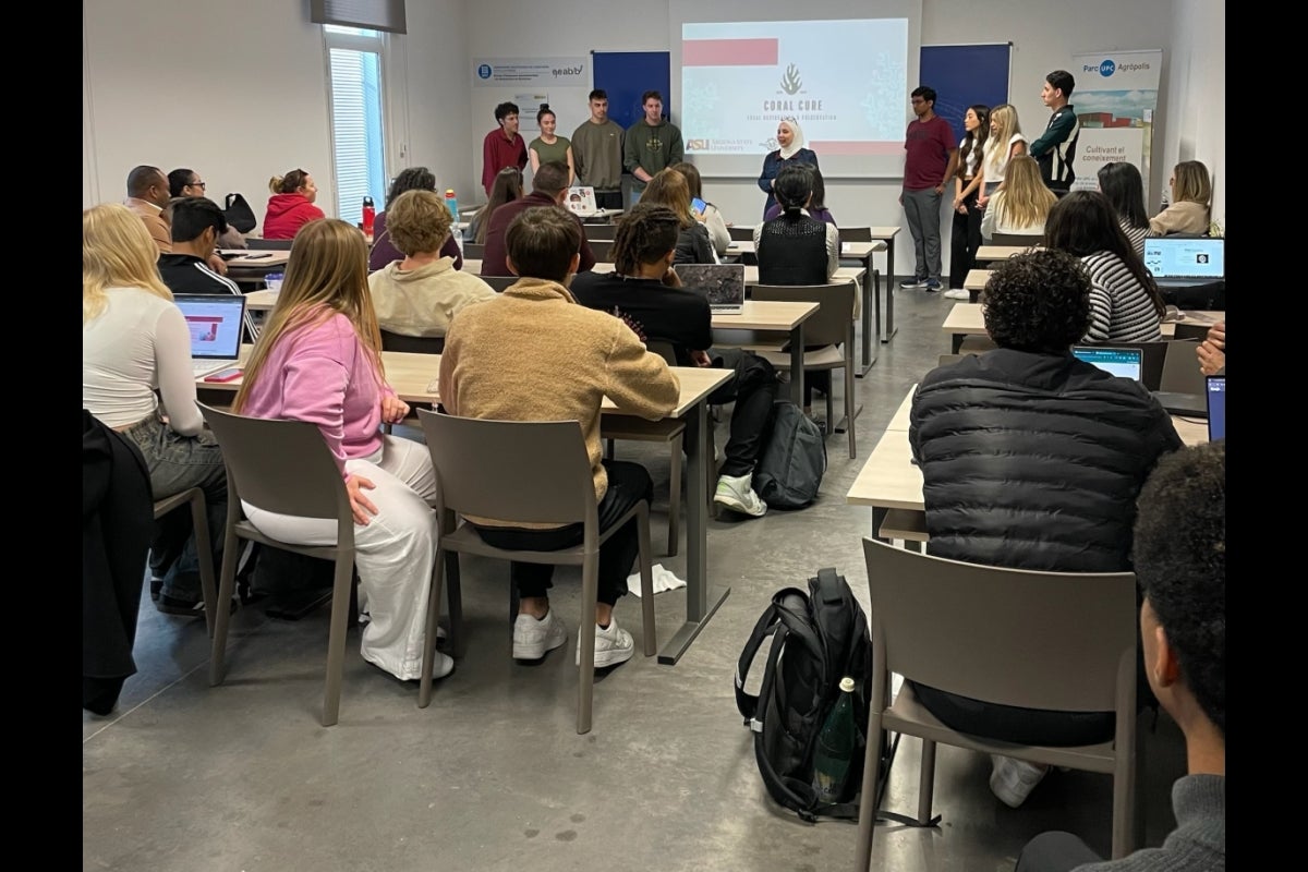 A group of people stand in front of a full classroom.