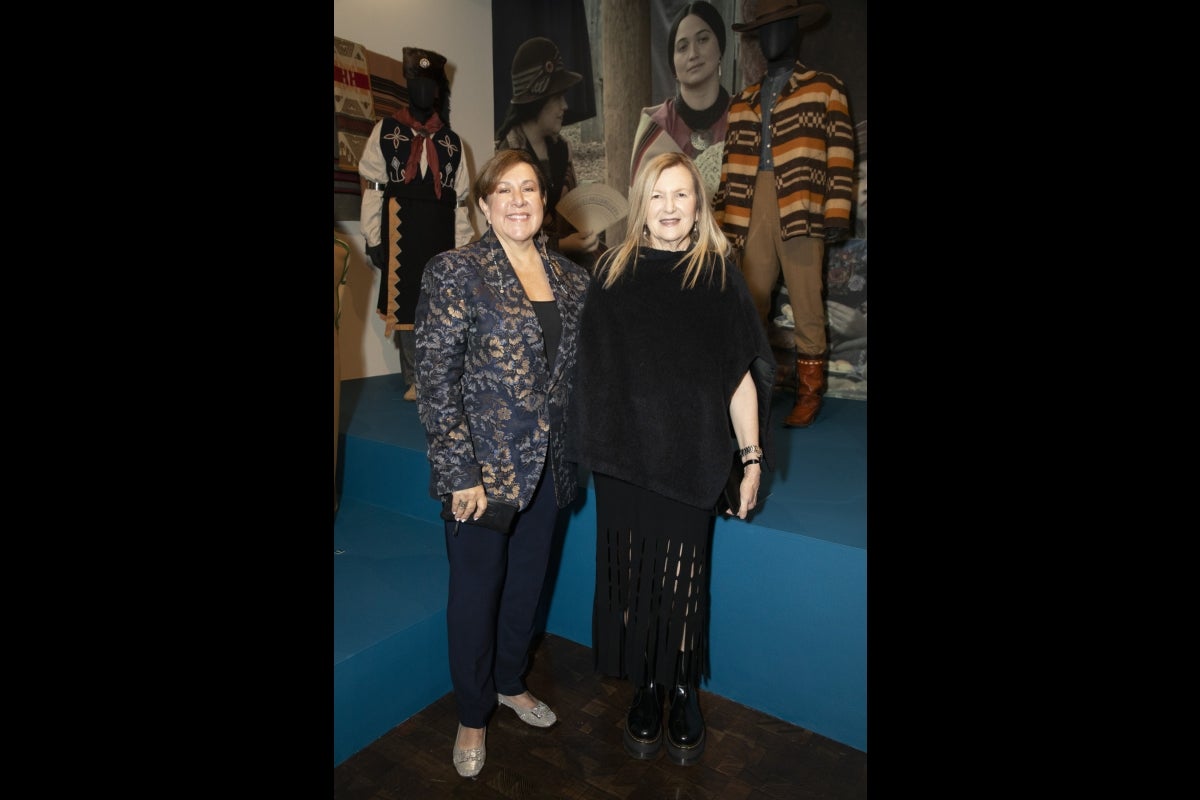 Two women smile in front of photos of a Native American woman.