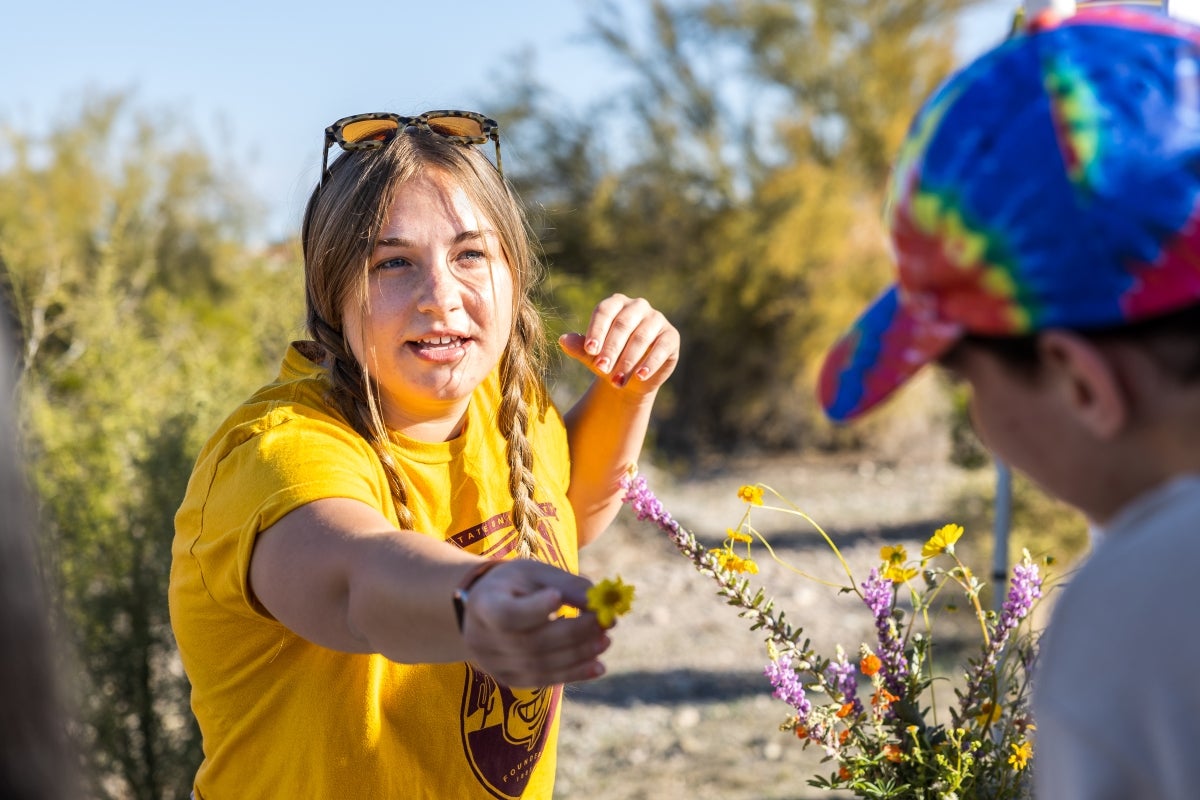 A woman holds a yellow flower out for a student to observe