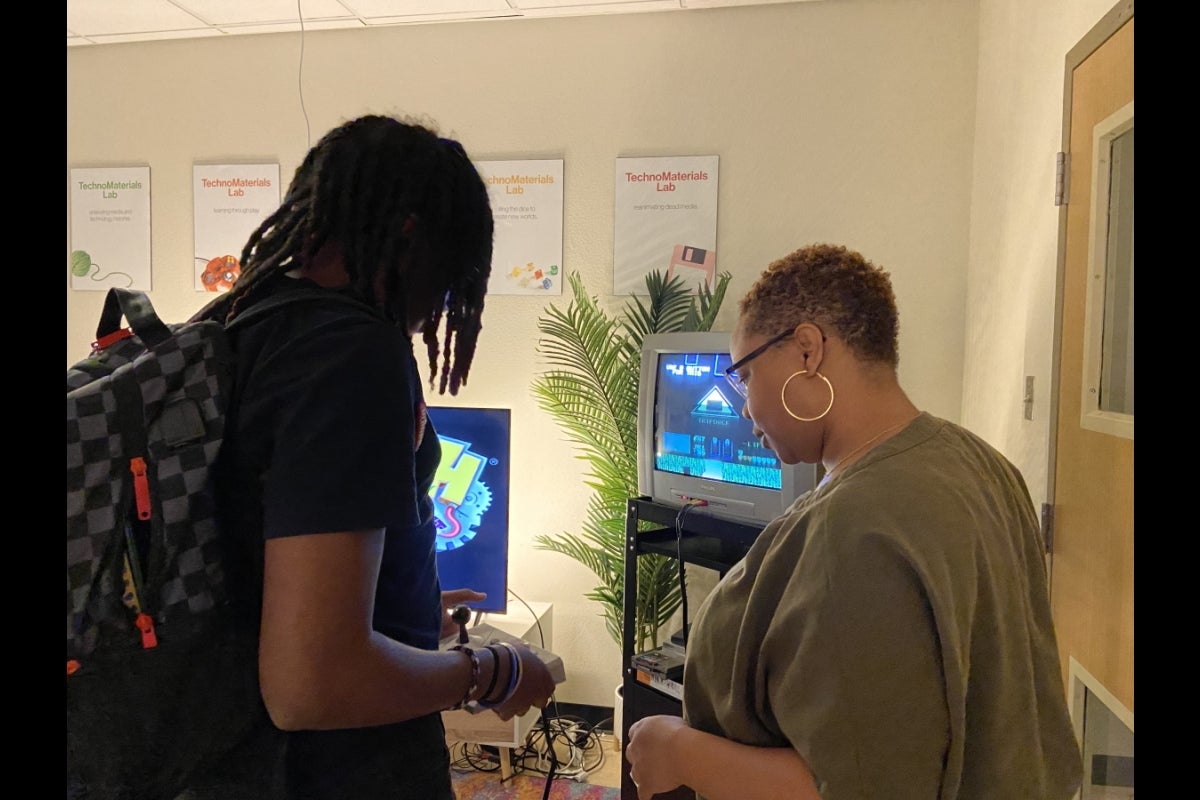 Two people look at the controller of a vintage gaming console. 