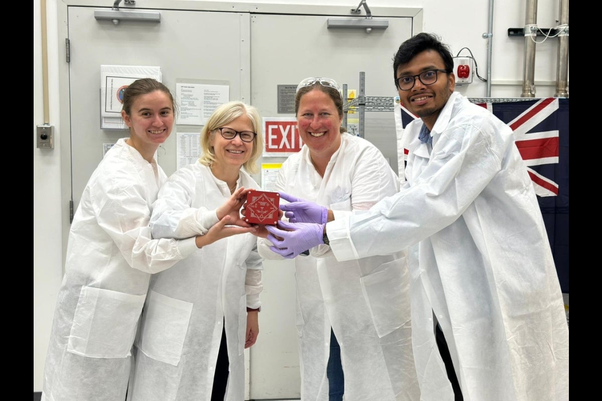 Four people holding a small red box dressed in white lab coats.