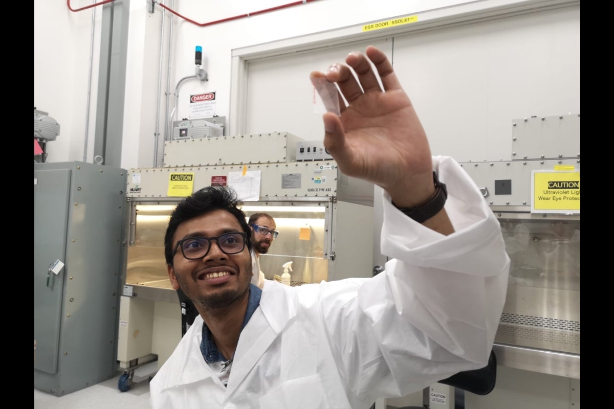 Man in white lab coat holding up a small see-through item