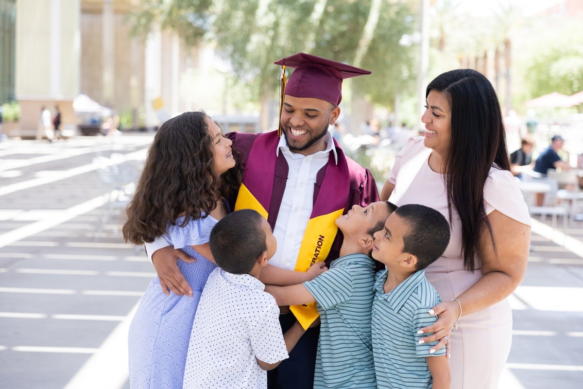 A mom and four little kids hug their dad in ASU graduation gear