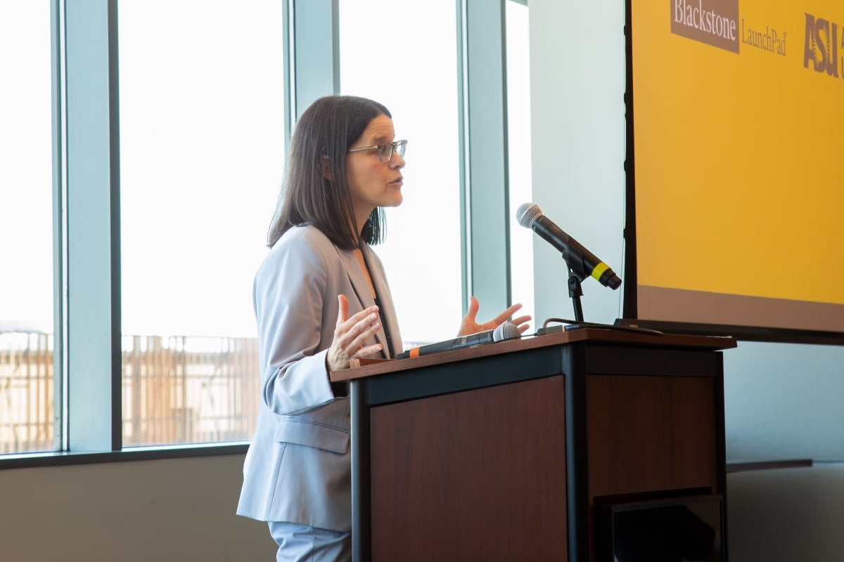 Woman stands at the podium speaking to a room of people