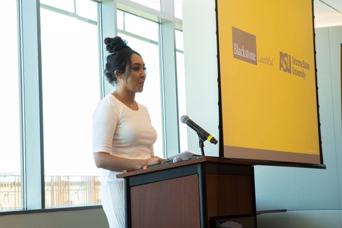 Woman stands at the podium speaking with a slide of the ASU and Blackstone LaunchPad logos on it