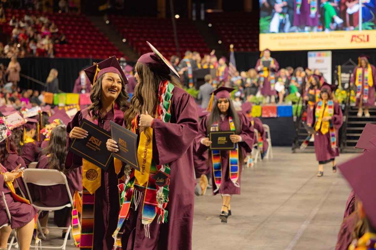 Graduates in maroon caps and gowns walking down aisle and talking after getting degree