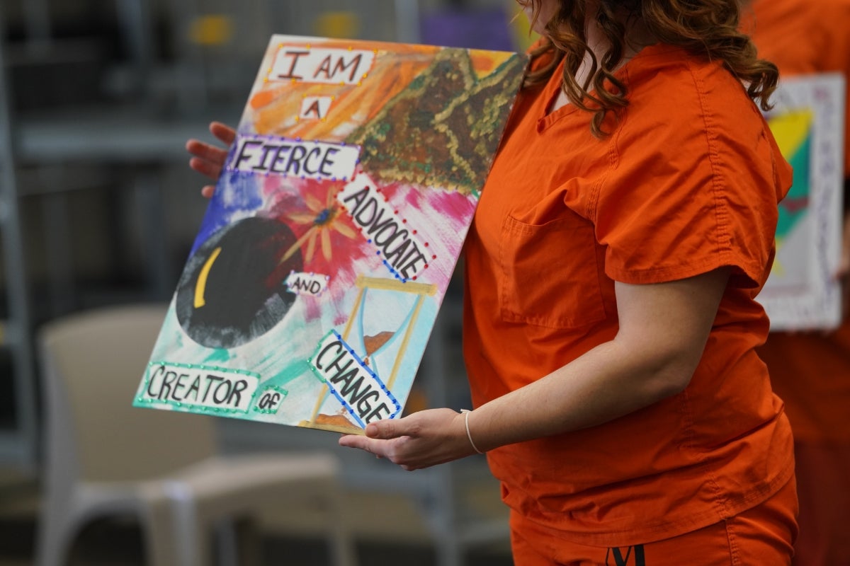 A woman holds up her painting that says, 