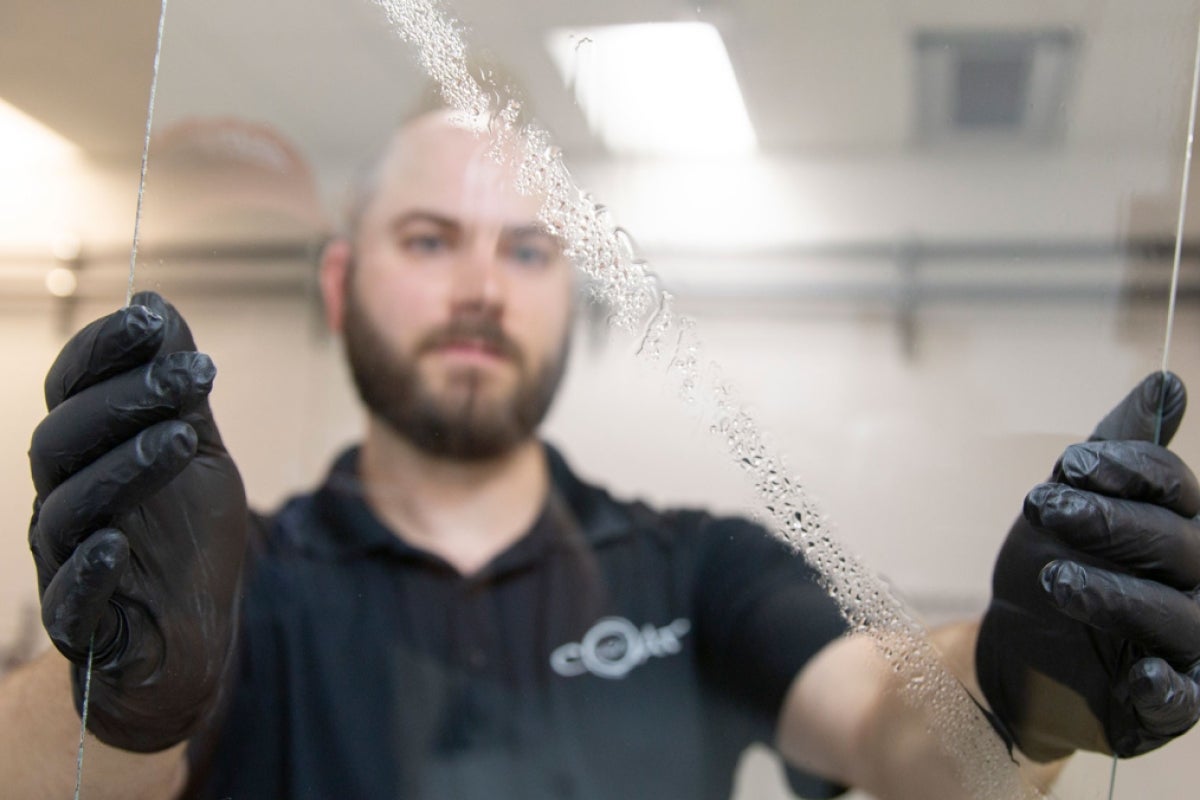 A man holds up a pane of glass with a strip of water on it