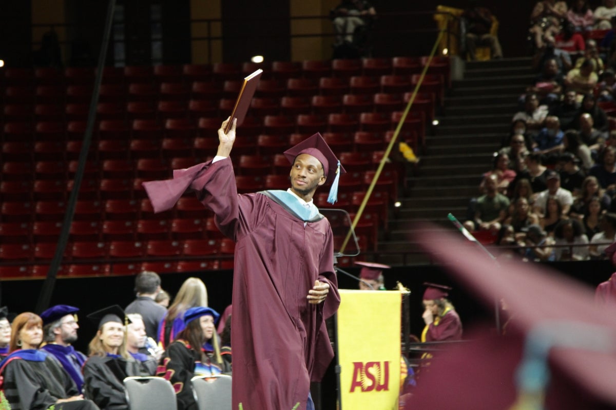 A graduate holds a diploma cover aloft