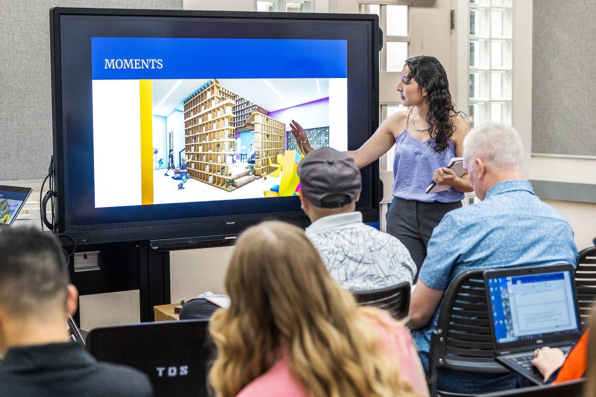 A young woman shows an illustration on a screen in a room full of people