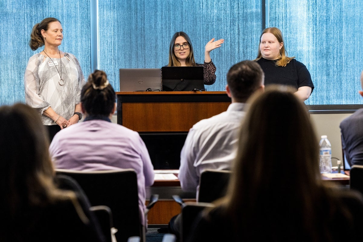 Three women stand in front of a room full of people