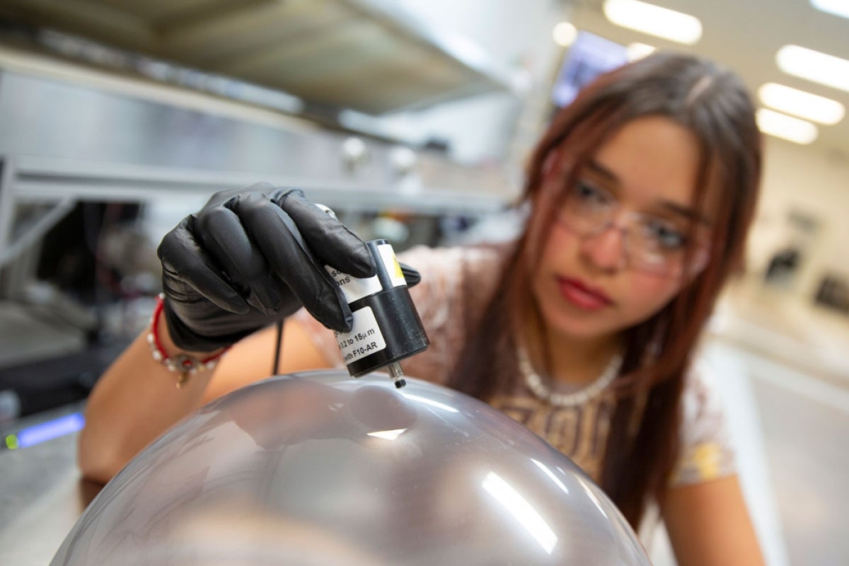 A woman holds a probe to a spacesuit helmet bubble