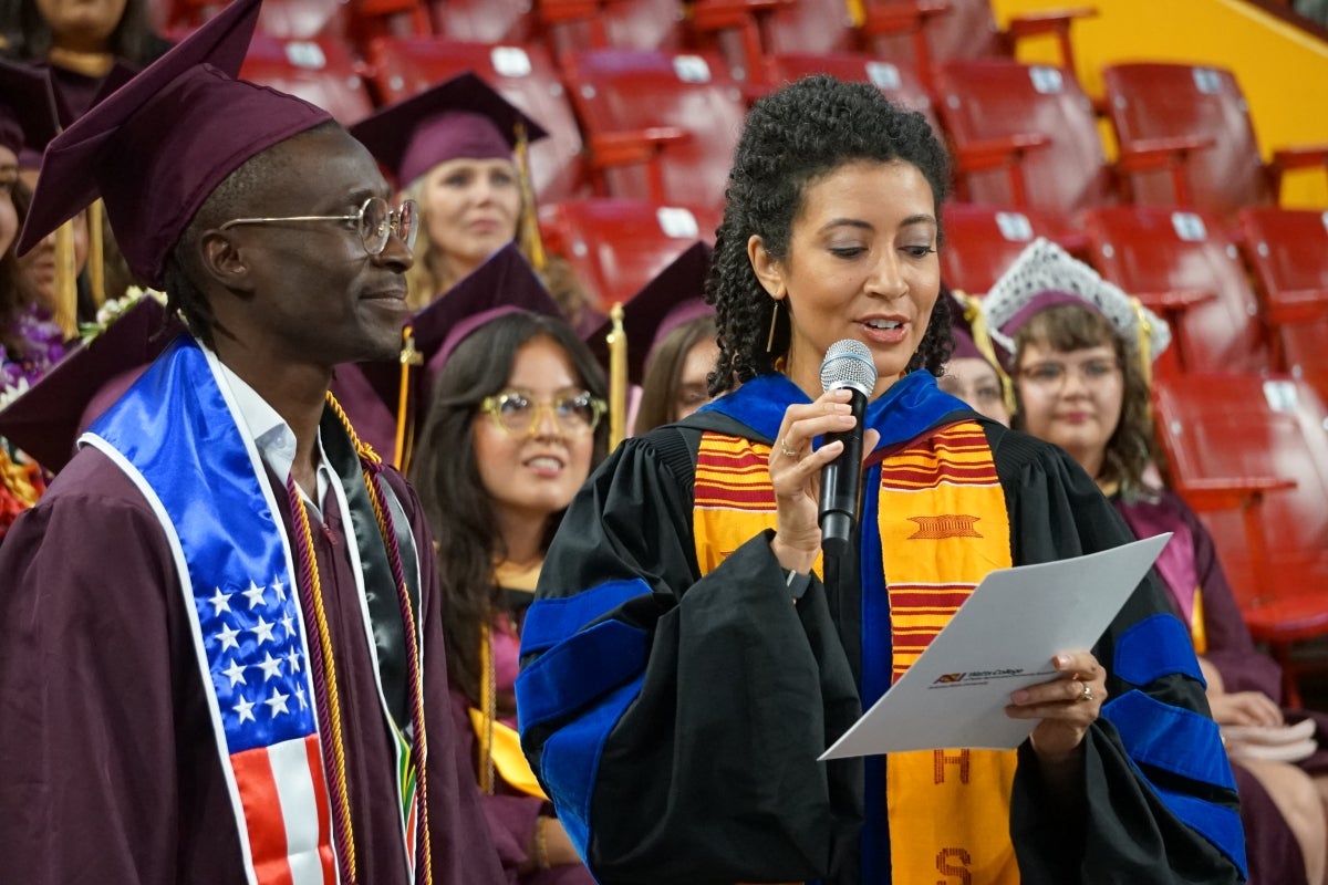 Woman speaks into microphone surrounded by graduates.