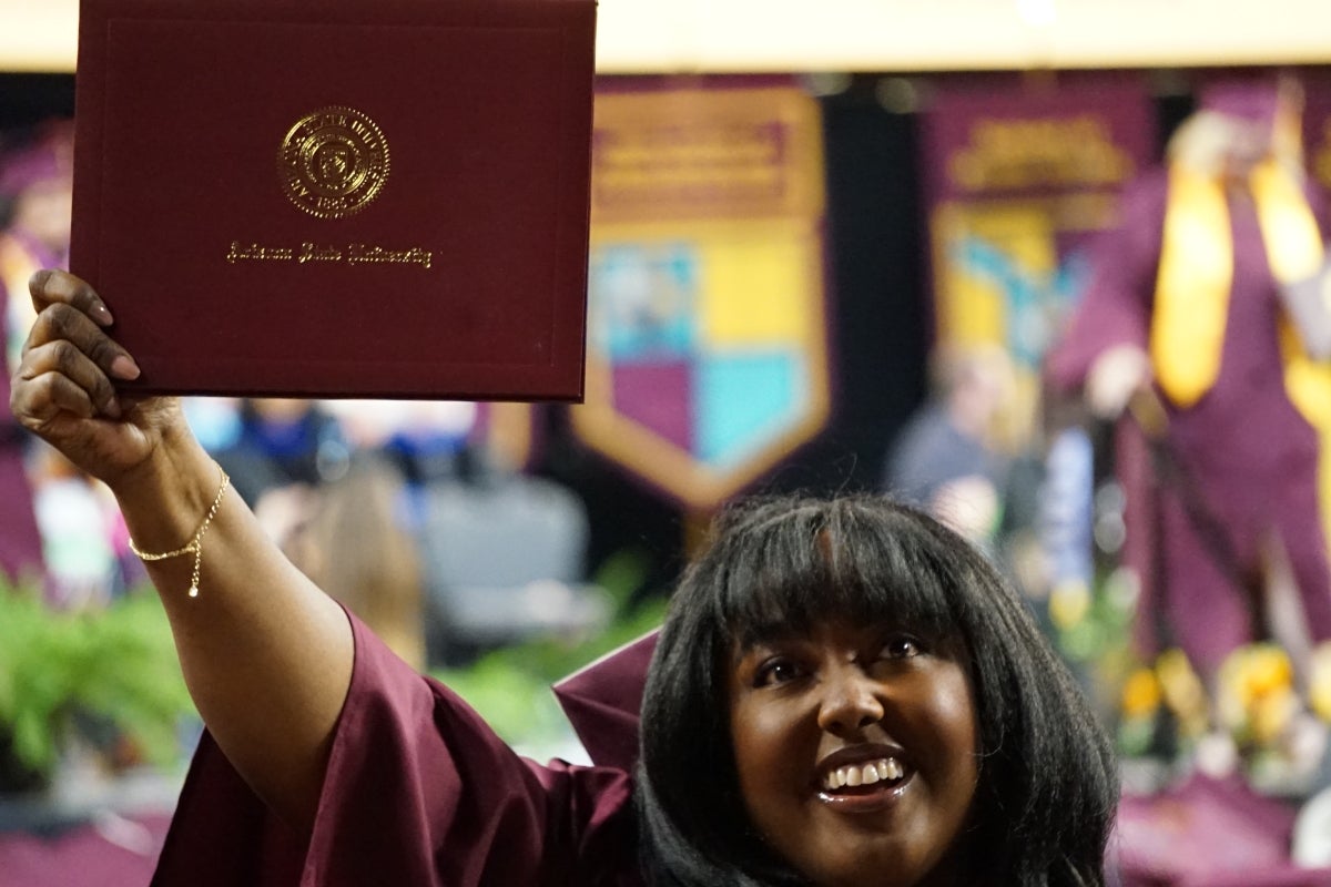 A graduate holds a diploma cover aloft