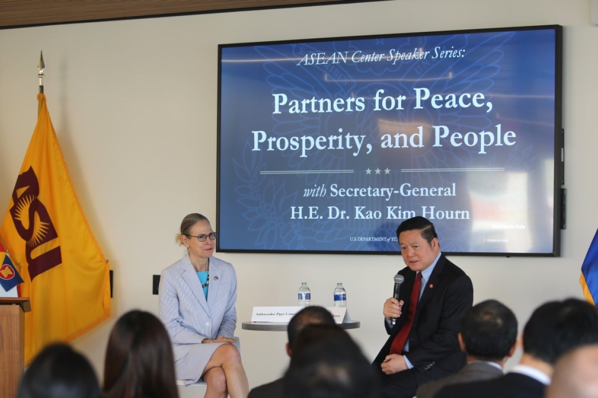 Piper Campbell sits next to Kao Kim Hourn, speaking to an audience