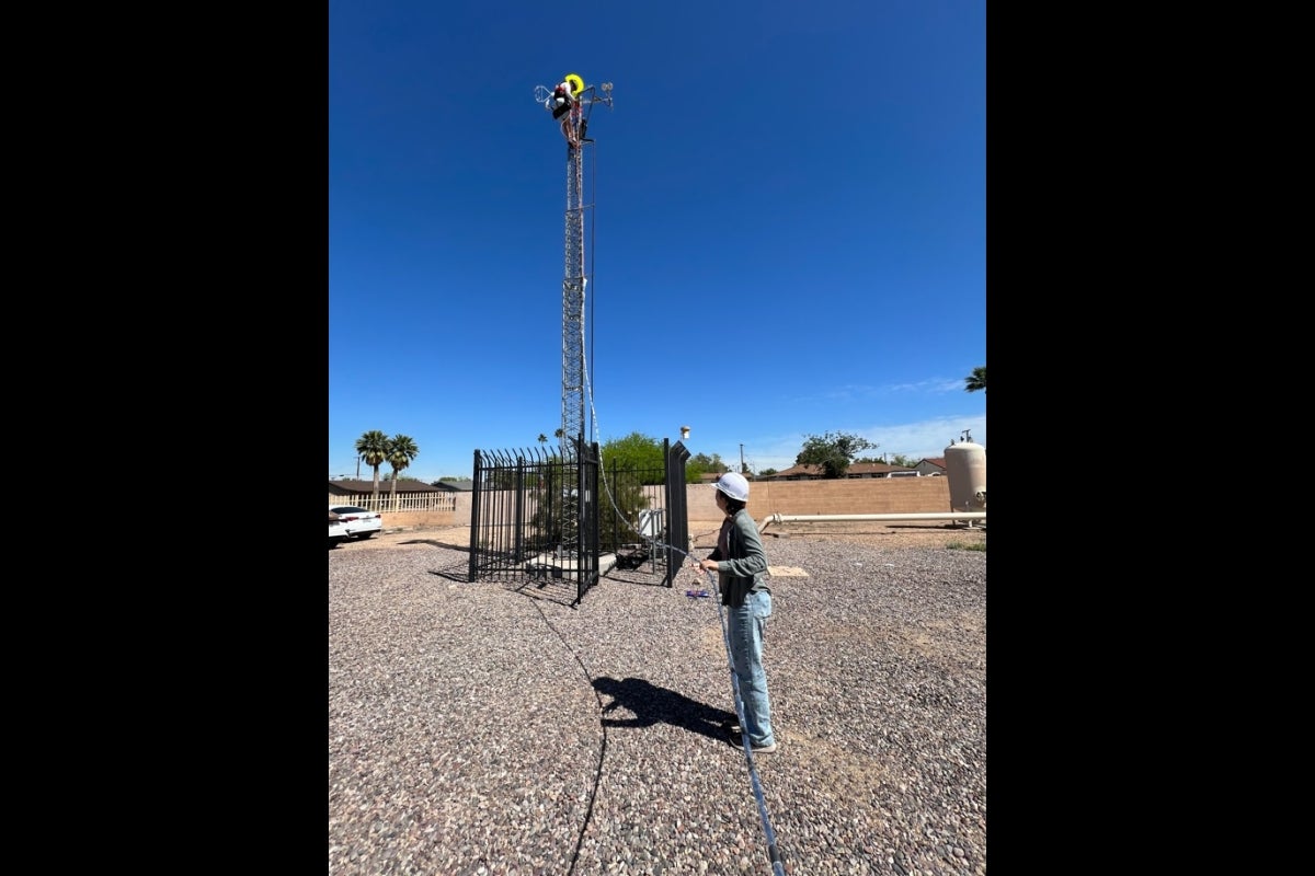 Man standing outdoors next to a large machine atop a 40-foot tower.