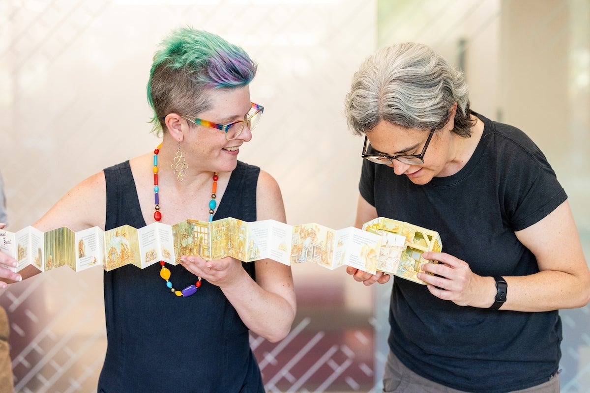 Two women smile while handling an accordian-like movable book.