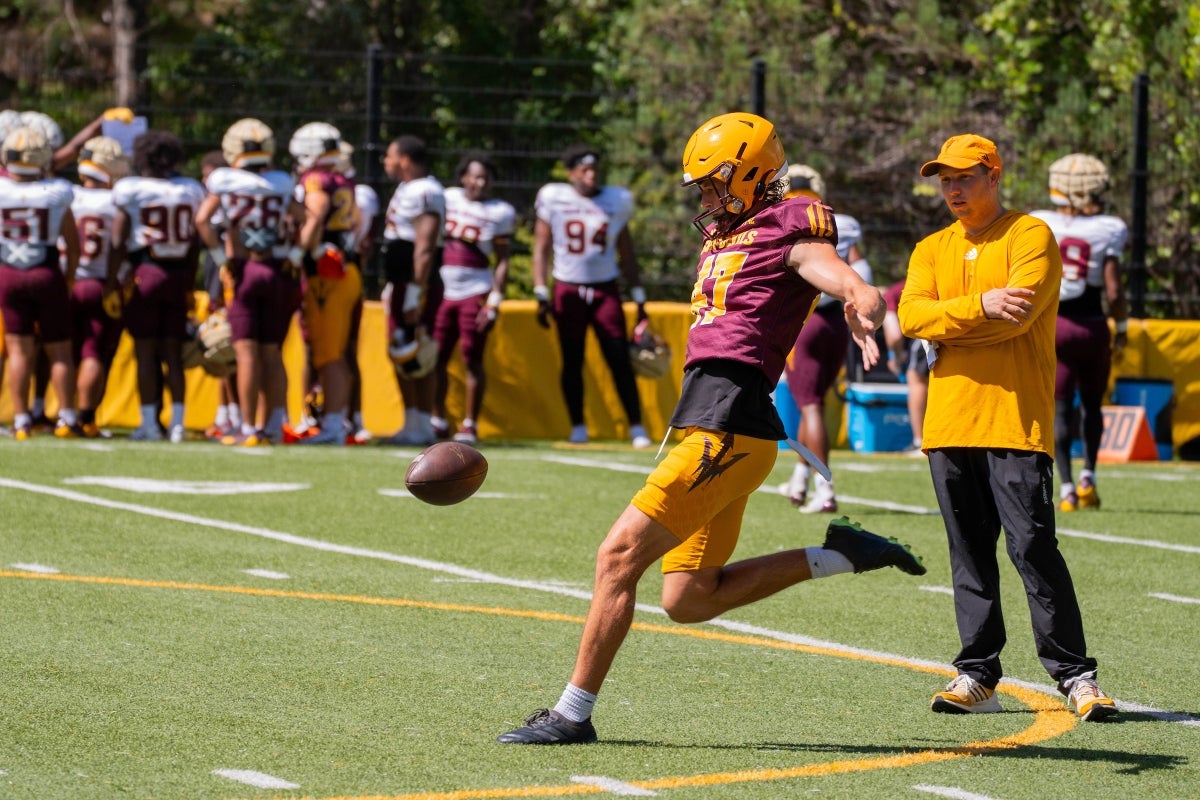 Football coach watches player punt the ball during practice