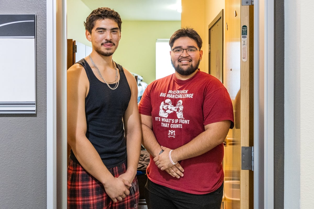 Two young men pose for a photo outside their new dorm room