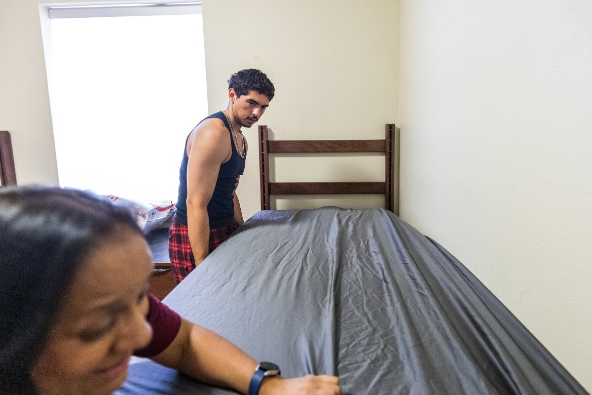 Mother and son make bed in dorm room