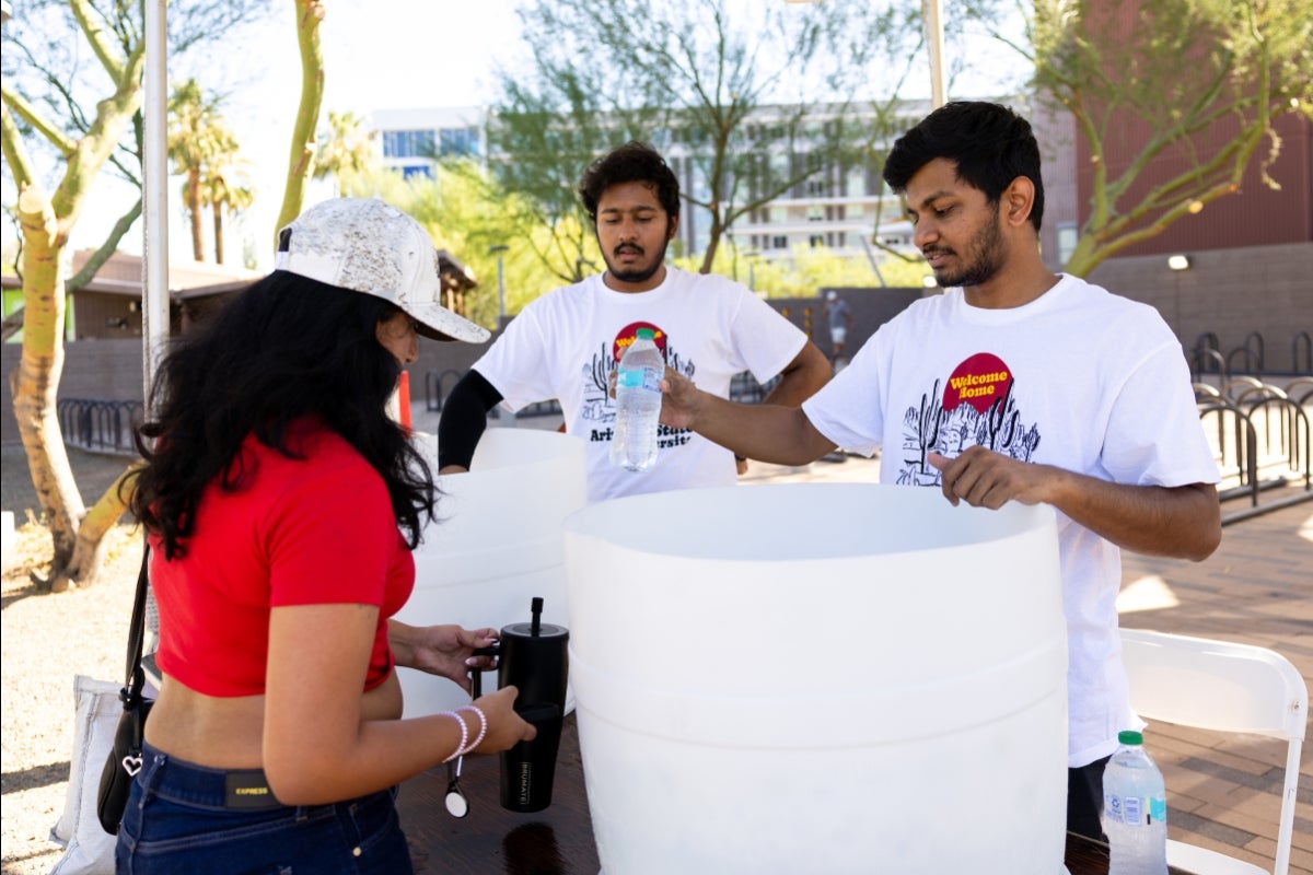 Two people hand out water to a student who is moving into campus